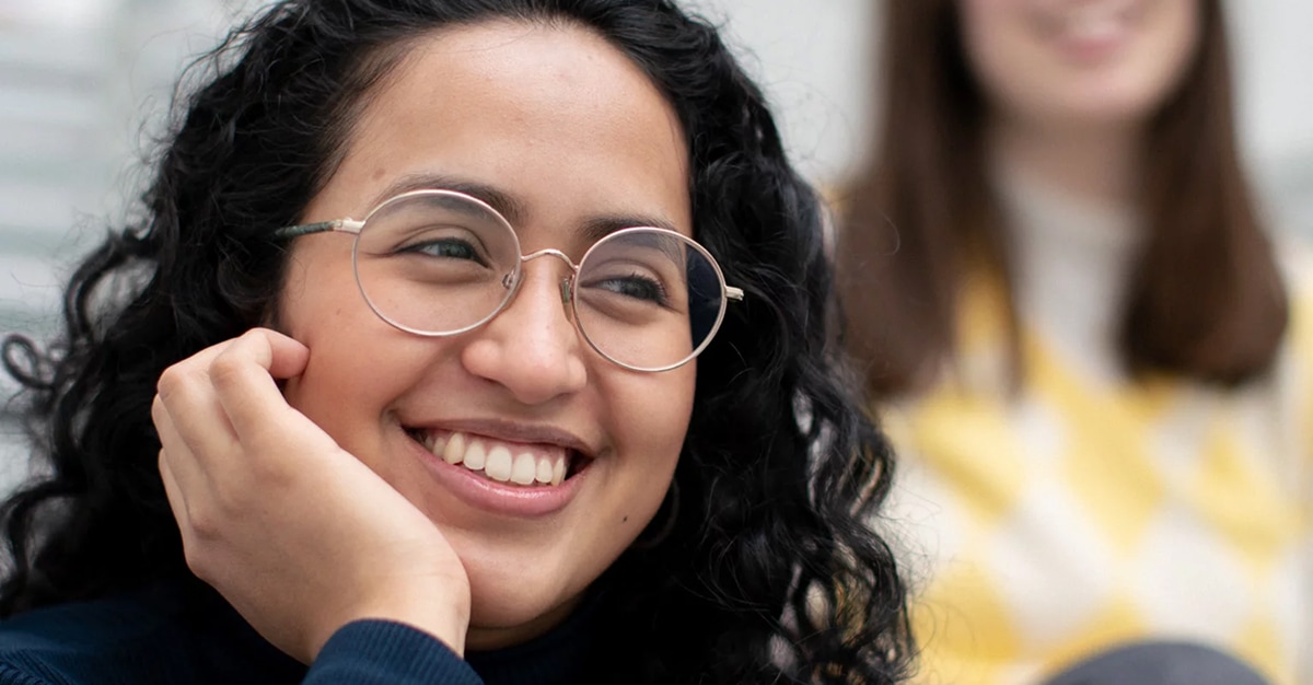Young woman with dark hair and round glasses, smiling and looking away (Brook stock imagery)