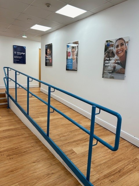 Interior wheelchair-access ramp with blue handrails and Invisalign / Bupa posters