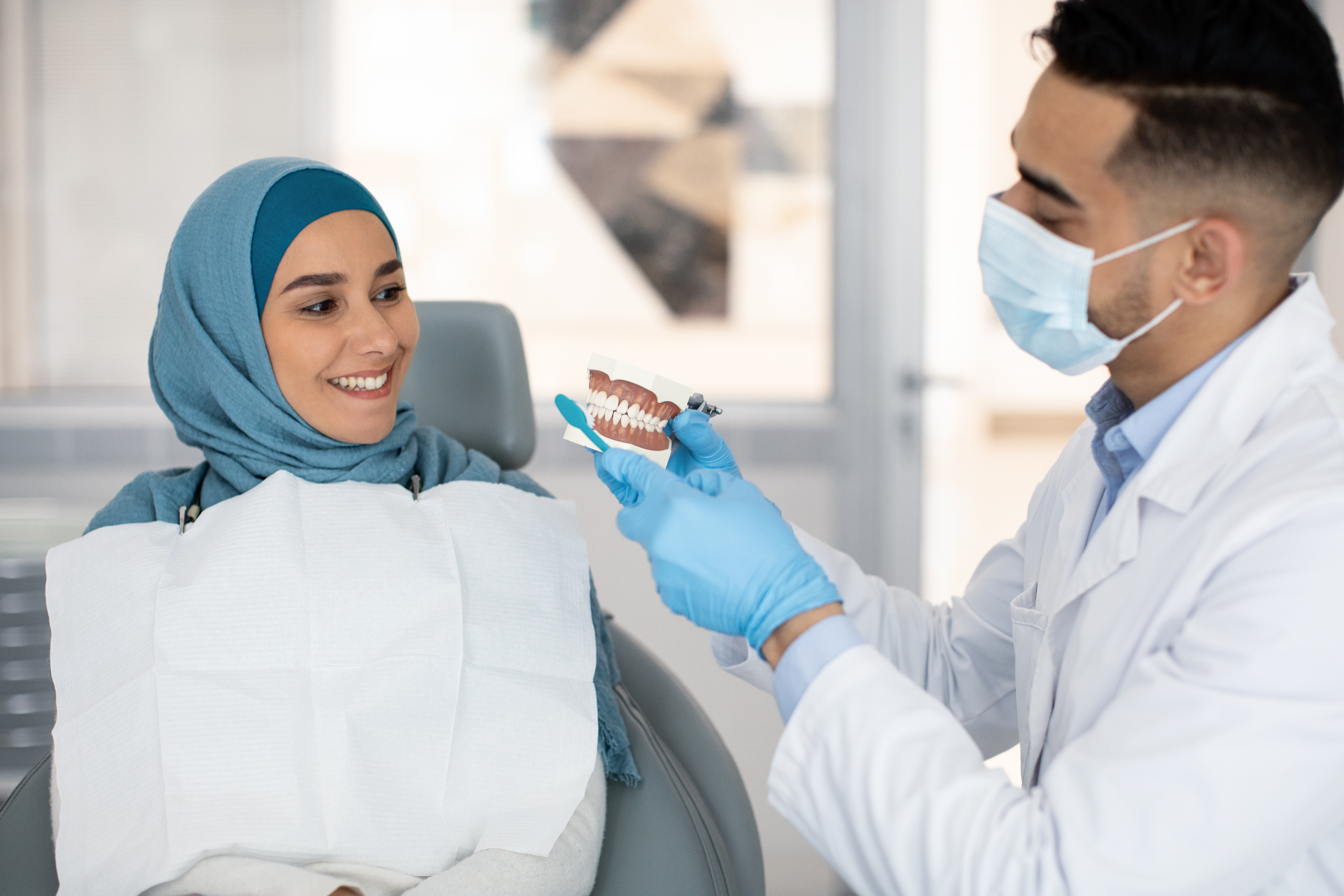 Male dentist holding jaw model explaining dental hygiene to a patient during a check up