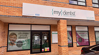 Exterior shopfront of mydentist, St. Luke's House, Emerson's Green, Bristol, with {my}dentist signage and NHS logo