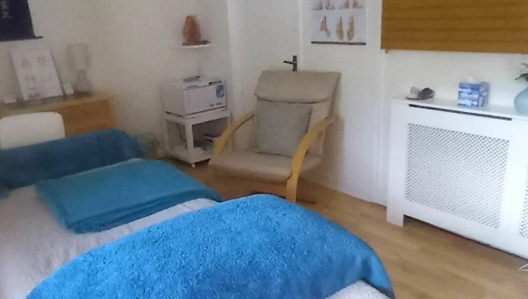 Treatment room interior with reclining chair, treatment couch with blue throws and foot reflexology charts on the wall